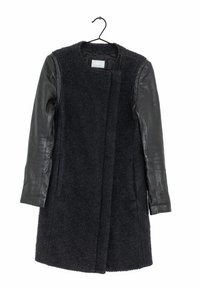 Abrigo negro con cuerpo de lana y mangas de cuero, con un escote redondo, frente abierto y dos bolsillos laterales. Tejido texturizado y cuero suave.