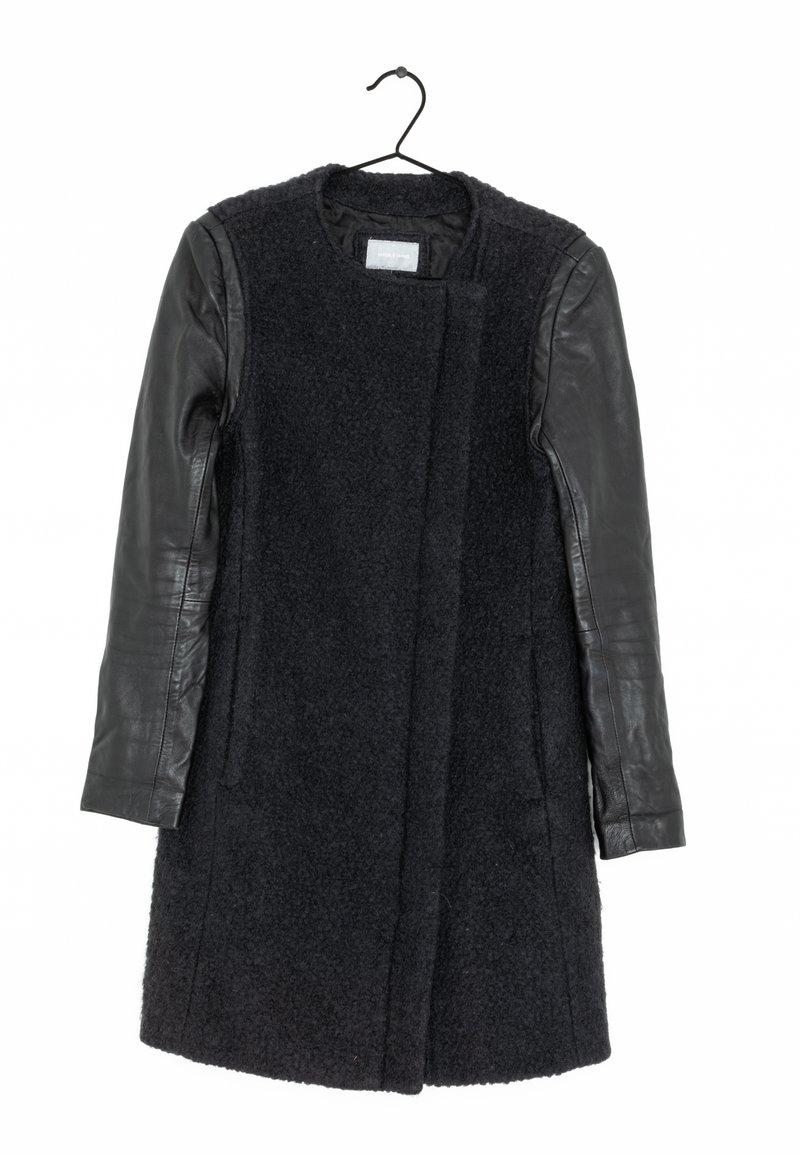 Abrigo negro con cuerpo de lana y mangas de cuero, con un escote redondo, frente abierto y dos bolsillos laterales. Tejido texturizado y cuero suave.
