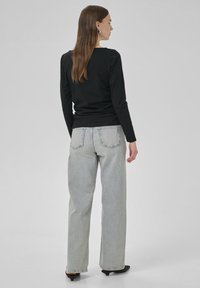Svart långärmad topp kombinerad med ljusblå vida jeans, med bakfickor och rak passform, mot en enfärgad bakgrund.