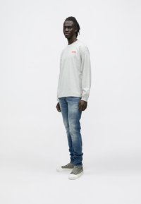 Harmaa pitkähihainen t-paita punaisella logolla, yhdistetty vaaleanpesuihin farkkuihin ja vihreisiin lenkkareihin. Yksinkertainen malli, istuva siluetti.