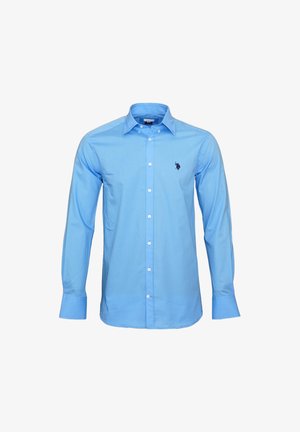 Chemise bleue claire à manches longues avec col pointu, présentant un petit logo brodé sur le côté gauche de la poitrine et une texture de tissu lisse.