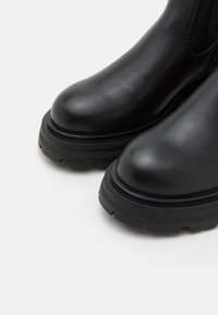 Svarta läder ankle boots med rundade tår, tjocka gummisålar och texturerad ovandel. Sömsyning längs sidorna.