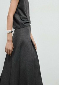 Jupe grise, longueur genoux, en tissu doux, avec une finition lisse et une forme évasée. Assortie à un haut à col rond et à un bracelet manchette en argent.