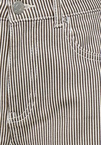 Tissu de pantalon rayé verticalement marron et blanc avec couture détaillée, bouton métallique et rivet près de l'ouverture de la poche.