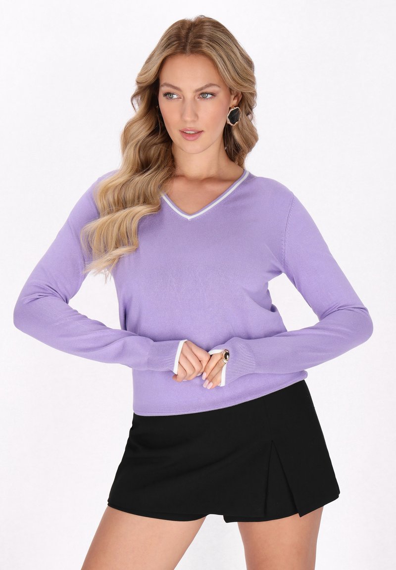 Lila V-Ausschnitt-Pullover mit langen Ärmeln, verziert mit weißen Akzenten am Halsausschnitt und an den Bündchen, kombiniert mit einem schwarzen, gefällteten Minirock.