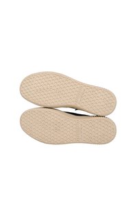 Semelles de chaussures noires avec un fond en caoutchouc beige texturé présentant un motif alvéolé et une marque en relief. Bords lisses et forme arrondie.