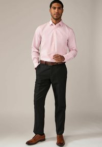 Camisa de vestir rosa claro con cuello, cierre de botones y mangas largas, combinada con pantalones negros y zapatos de cuero marrón.