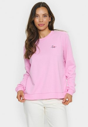 Lichtroze sweatshirt met lange mouwen, ronde hals en ribgebreide manchetten. Heeft een kleine "love" grafiek in zwart en rood op de borst.