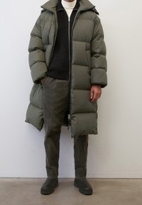 Person wearing long olive green puffer coat, black sweater over white turtleneck, olive corduroy pants, and dark green boots.