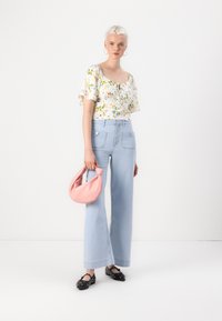 Top bianco floreale con maniche corte a volant, jeans a gamba larga azzurri, borsa rosa e scarpe nere con dettagli decorativi.