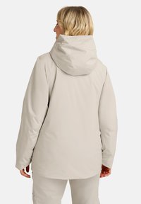Veste imperméable beige clair avec capuche, présentant une texture lisse, des manches longues et une coupe décontractée. Aucun fermoir visible ni motifs.