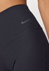 Primo piano di una persona che indossa leggings neri a coste a vita alta con il logo swoosh grigio di Nike vicino alla vita.