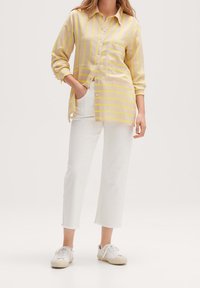 Button-up shirt in yellow and pink stripes, featuring a chest pocket, paired with white cropped pants and white sneakers.