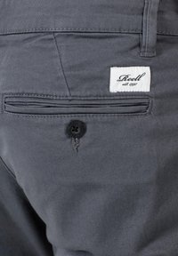 Pantalones grises con una textura suave, que presentan un bolsillo trasero con un botón negro y una etiqueta de marca blanca cosida encima.