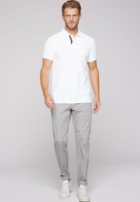 Polo bianco a maniche corte con dettagli neri, abbinato a pantaloni chinos grigi chiari e scarpe da ginnastica bianche. Tessuto morbido.