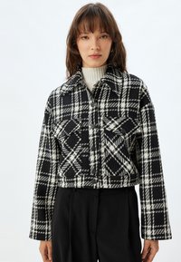 Tjekket sort og hvid cropped jakke med stor krave, frontknapper og to brystlommer. Vævet tekstur med plaidmønster.
