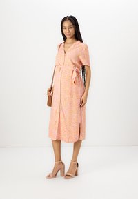 Pink and orange patterned midi dress with short sleeves, cinched waist, and front button closure. Paired with tan block-heel sandals.