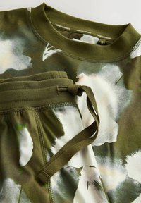 Oliwkowa bluza i spodnie w białe i zielone abstrakcyjne wzory kwiatowe, z prążkowanym okrągłym dekoltem i elastycznym pasem ze sznurkiem.