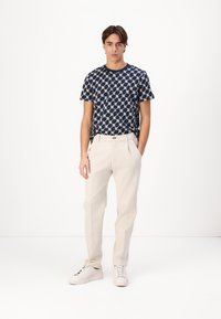 Marineblå kortermet T-skjorte med geometrisk mønster, paret med lysebeige tapered bukser og hvite joggesko. Enkel design, uformell passform.