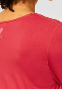 Červené bavlněné tričko s kulatým výstřihem, hladkým povrchem a krátkými rukávy. Obsahuje malý potisk.