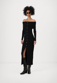 Svart ribbade off-shoulder klänning med långa ärmar, knappstängning framtill, revär upp till låret och parat med knähöga svarta stövlar.