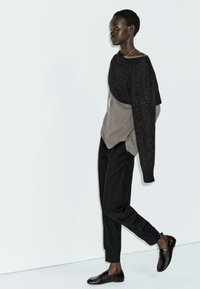 Oversized black and gray knit sweater with long sleeves, paired with tailored black trousers and black loafers, showcasing a relaxed fit.