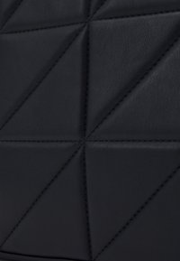 Černý kožený povrch s geometrickým trojúhelníkovým prošíváním, které tvoří prošívaný vzor.