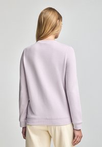 Sudadera de lavanda claro con cuello redondo, puños acanalados y dobladillo. Tejido suave con una textura lisa, cuenta con un diseño simple y minimalista.