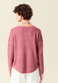 Różowy sweter dzianinowy z długimi rękawami, luźnym krojem i zaokrąglonym dołem. Miękka tekstura i lekko oversize'owy fason zwiększają komfort noszenia.