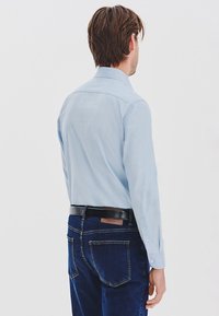 Jasnoniebieska koszula z kołnierzykiem i długimi rękawami, w połączeniu z ciemnoniebieskimi dżinsami. Posiada gładką tkaninę oraz czarny pasek z prostokątną klamrą.