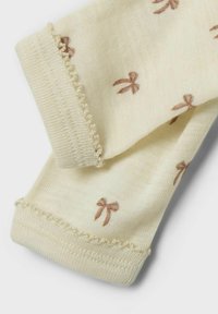 Chaussettes de couleur crème clair avec de petits motifs de nœuds marron, présentant une texture côtelée délicate et un bord festonné.