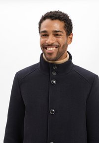 Marineblauer Wollmischungs-Mantel mit hohem Kragen, ausgestattet mit einer Fünf-Knopf-Verschluss und subtiler Textur. Akzentuiert durch einen hellbeigen Rollkragenpullover darunter.