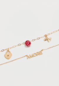 Deux bracelets en or, l'un avec une perle à pois rouges et des breloques en forme de cœur et de nœud dorés, l'autre avec une breloque portant le mot "AMORE" sur un fond blanc.
