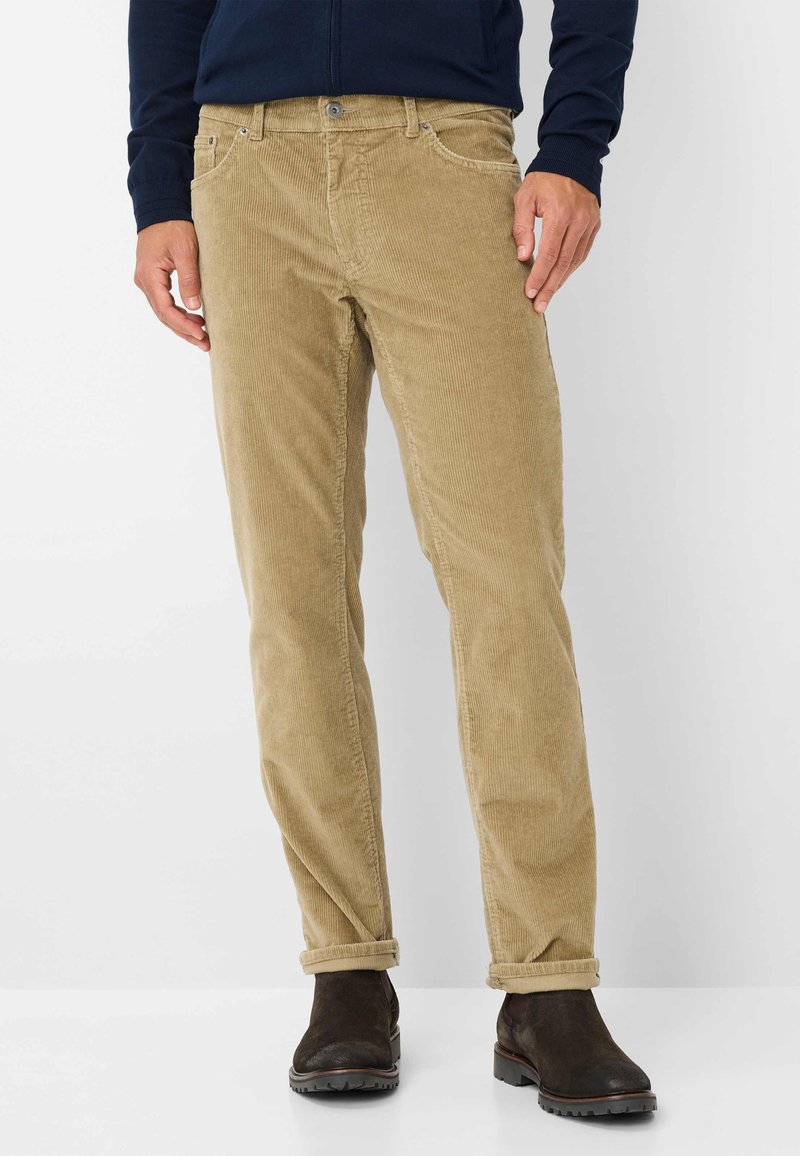 Pantaloni in corduroy beige con taglio dritto, caratterizzati da una texture a coste, orli arrotolati e tasche frontali. Indossati con stivaletti neri alla caviglia.