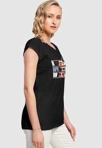Sort T-shirt med korte oprulbare ærmer, der har et grafisk design af fire farverige øjne i forskellige stilarter over fronten.