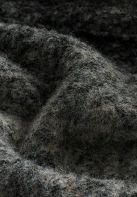 Szaro-czarna teksturowana tkanina o miękkim, puszystym wyglądzie. Charakteryzuje się połączeniem włókien, które tworzą warstwową i lekko falistą powierzchnię.