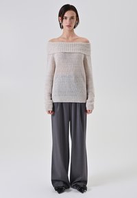 Maglione a maglia scollo a barca in beige chiaro, con collo a coste e maniche lunghe, abbinato a pantaloni a gamba larga grigi e scarpe nere con punta appuntita.
