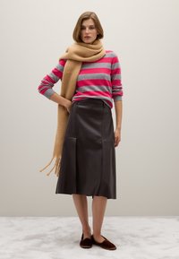 Maglione a strisce grigio e rosa, sciarpa beige, gonna midi in pelle nera e pantofole marroni. Texture morbide e vestibilità su misura.