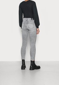 Grå högmidjade slim fit-jeans med en urtvättad finish, sidostrecker och en märkesresår, i kombination med svarta ankelboots.