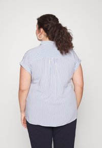 Camisa de manga corta, abotonada, en rayas azul claro y blanco. Presenta un collar, pliegue trasero y dobladillo redondeado. Tejido de mezcla de algodón.