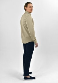 Beige polo shirt met lange mouwen en kraag, gecombineerd met donkerblauwe broek en zwarte instap schoenen. Effen kleur, gladde textuur.