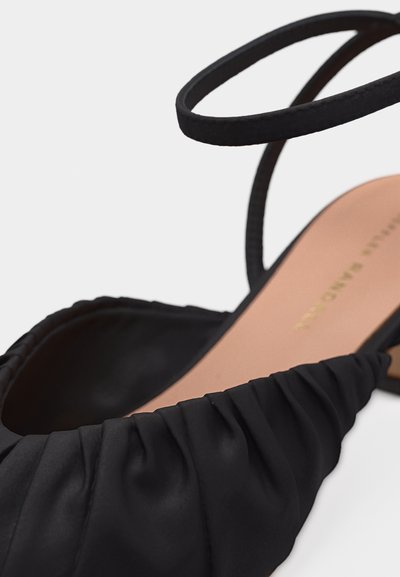 Μαύρο δερμάτινο σανδάλι με ραβδώσεις, λεπτό λουράκι στον αστράγαλο και ταμπά εσωτερική σόλα με χρυσό λογότυπο, εμφανίζεται σε κοντινή λεπτομέρεια.