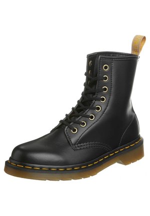 Botte montante en cuir noir à lacets, avec surpiqûres jaunes, semelle translucide marron et languette en tissu jaune à l'arrière.