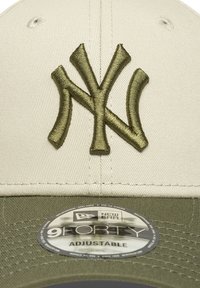 Cappellino da baseball beige con logo ricamato "NY" in verde oliva, visiera piatta e fascia regolabile. Presenta un'etichetta New Era 9FORTY.