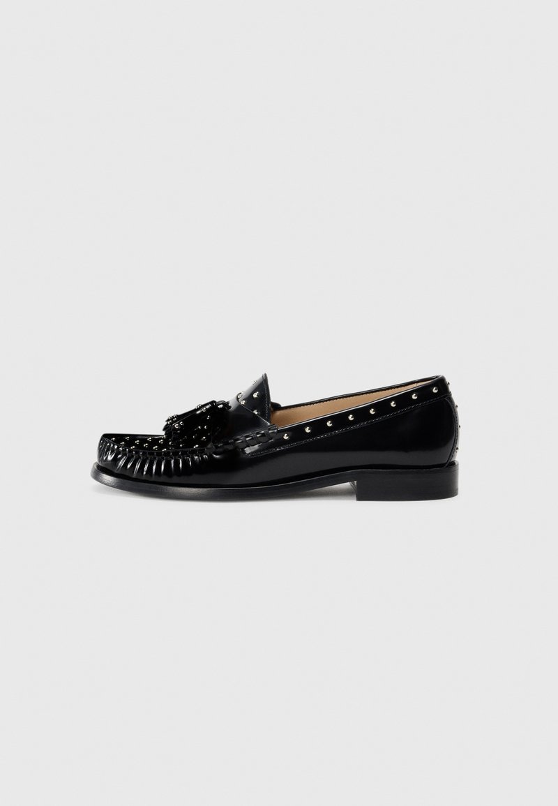 Mocassins en cuir noir avec des coutures décoratives, des clous en métal le long du dessus, un talon bas et un accent en forme de nœud texturé à l'avant.