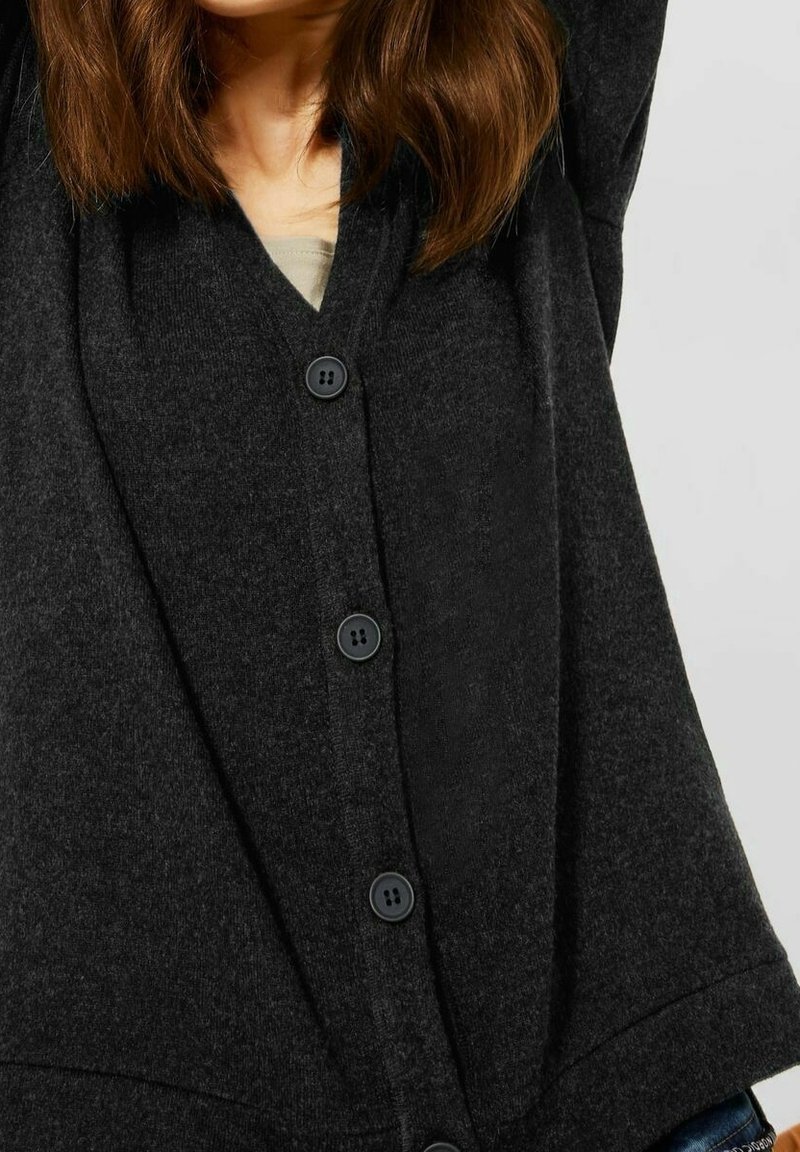 Černý kardigan s výstřihem do V, vyrobený z měkkého materiálu. Má knoflíkovou přední část se čtyřmi velkými knoflíky a volné rukávy.