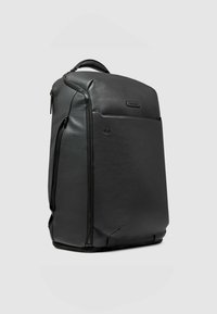 Zwarte leren rugzak met een afgeronde bovenkant, een gladde textuur, een voorvak met ritssluiting en een gewatteerd handvat om te dragen.