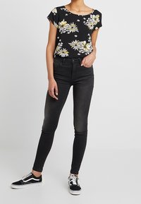 Sort blomstermønstret top med gule og hvide blomster, parret med sorte skinny jeans og sorte sneakers med hvide detaljer.