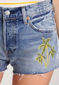 Jeansshorts med franskant, ljusblå färg och broderade gula palmer på vänster sida. Har en framficka och metallknapp.