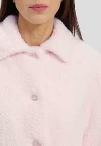 Chaqueta rosa esponjosa con cuello muesca, que presenta botones transparentes y una textura suave. Vista en primer plano que destaca los detalles del material.